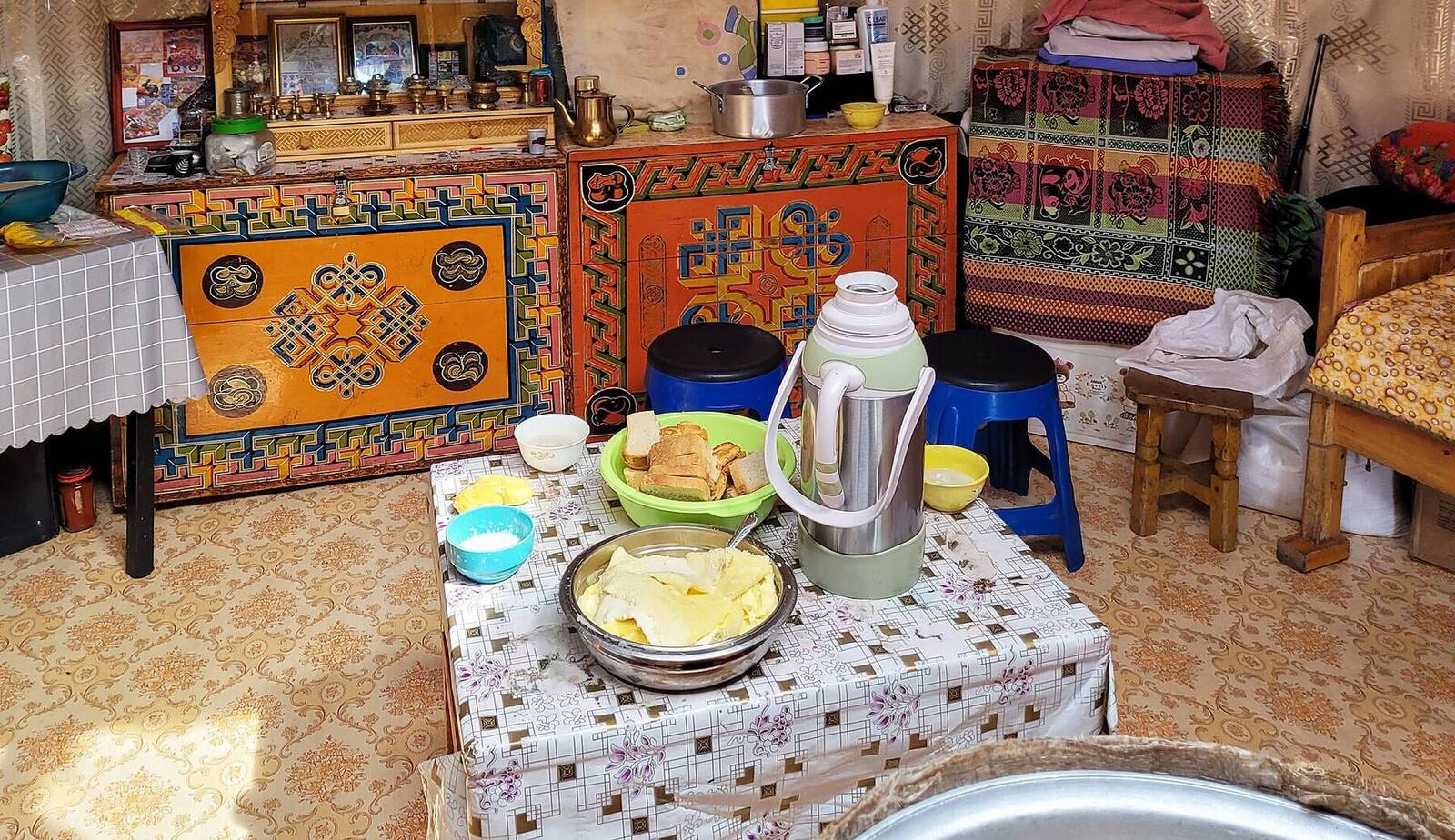 Inside a family ger: painted orange furniture, a stove and a table set with bread and milk tea